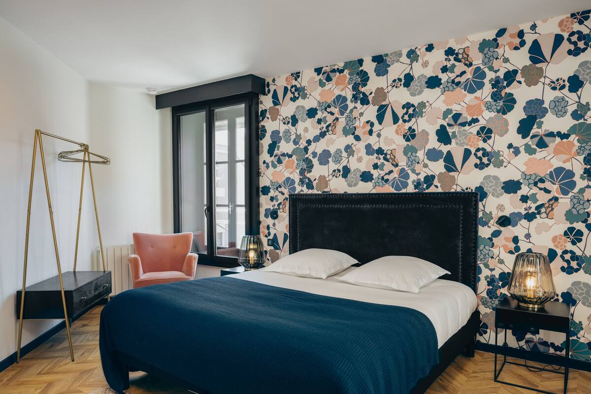 A bedroom with a bed, a chair, a floor lamp, and a nightstand.