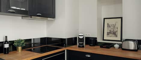 A modern kitchen with black cabinetry, a built-in stove, a coffee maker, and a framed picture on the wall.
