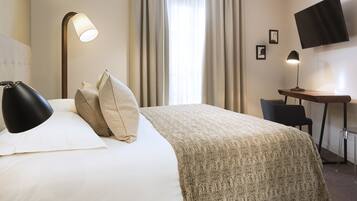 A hotel room with a bed, two bedside lamps, a desk with a chair, a flat-screen TV, and curtains.