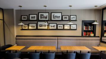 A modern interior with a long bench seating area, multiple tables, and a wall adorned with framed photographs.