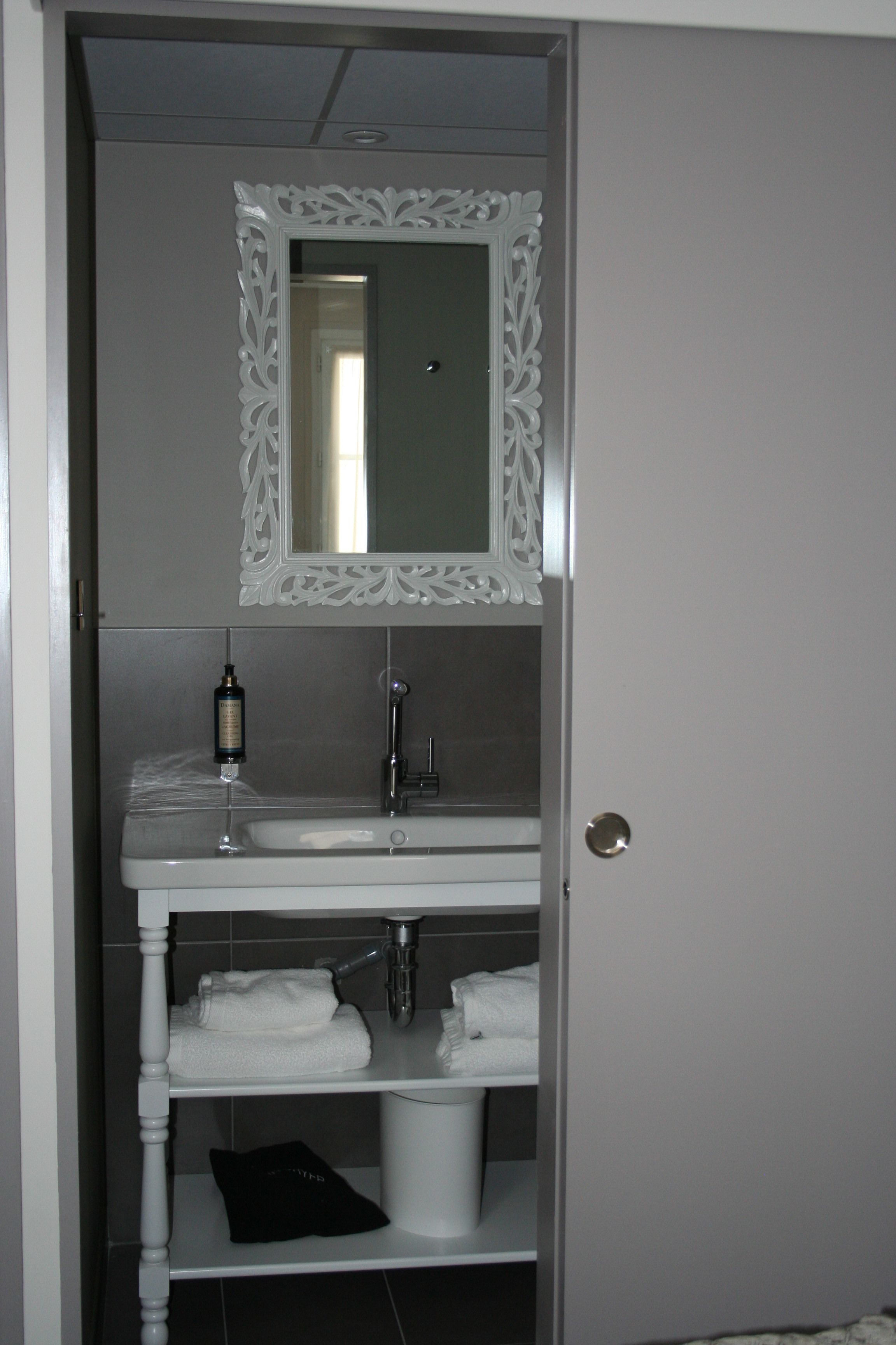 A bathroom with a white vanity, a mirror with an ornate frame, a sink, and a toilet.