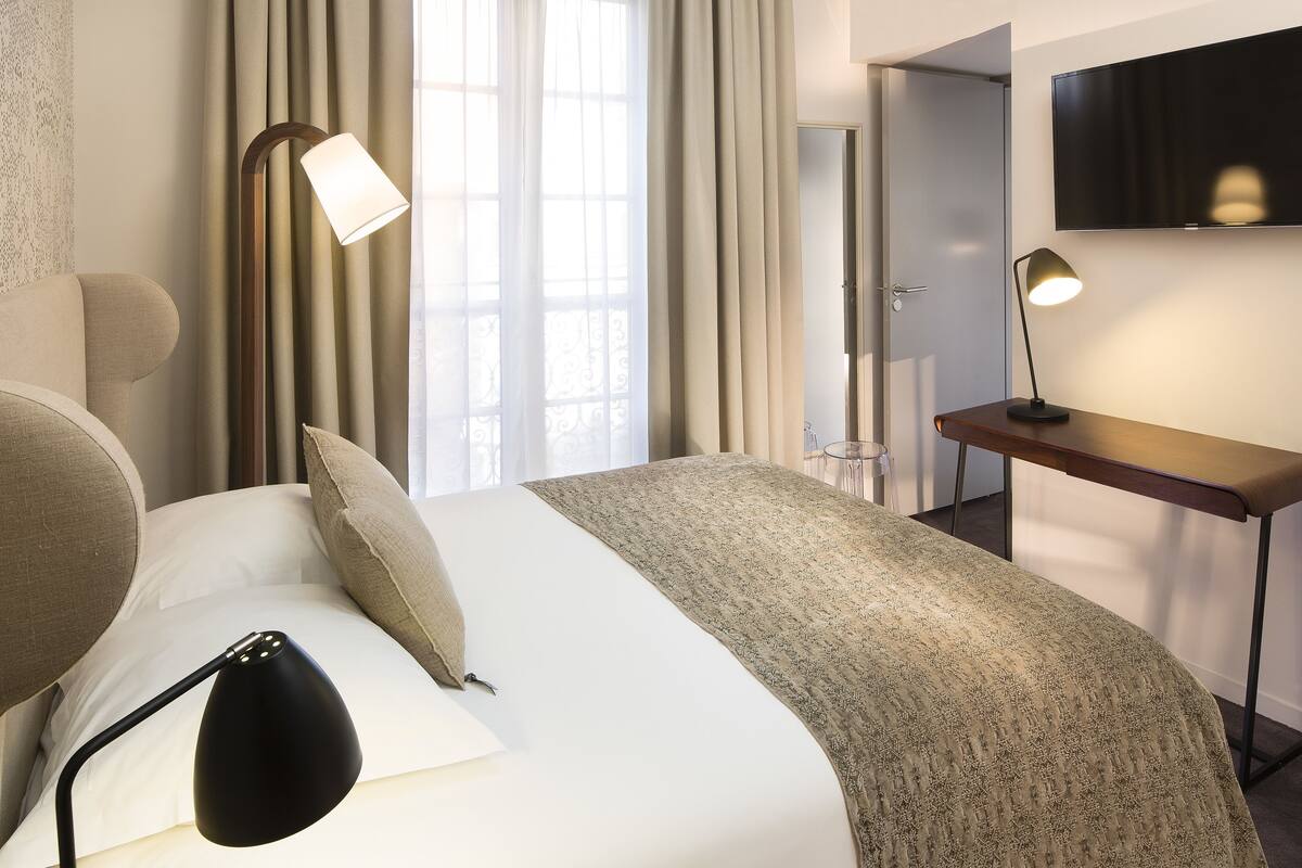 A hotel room with a bed, a desk, a chair, a TV, and a lamp.
