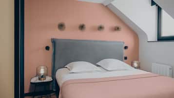 Une chambre avec un plafond en pente, un lit recouvert de draps blancs, une couverture rose et deux lampes de chevet.