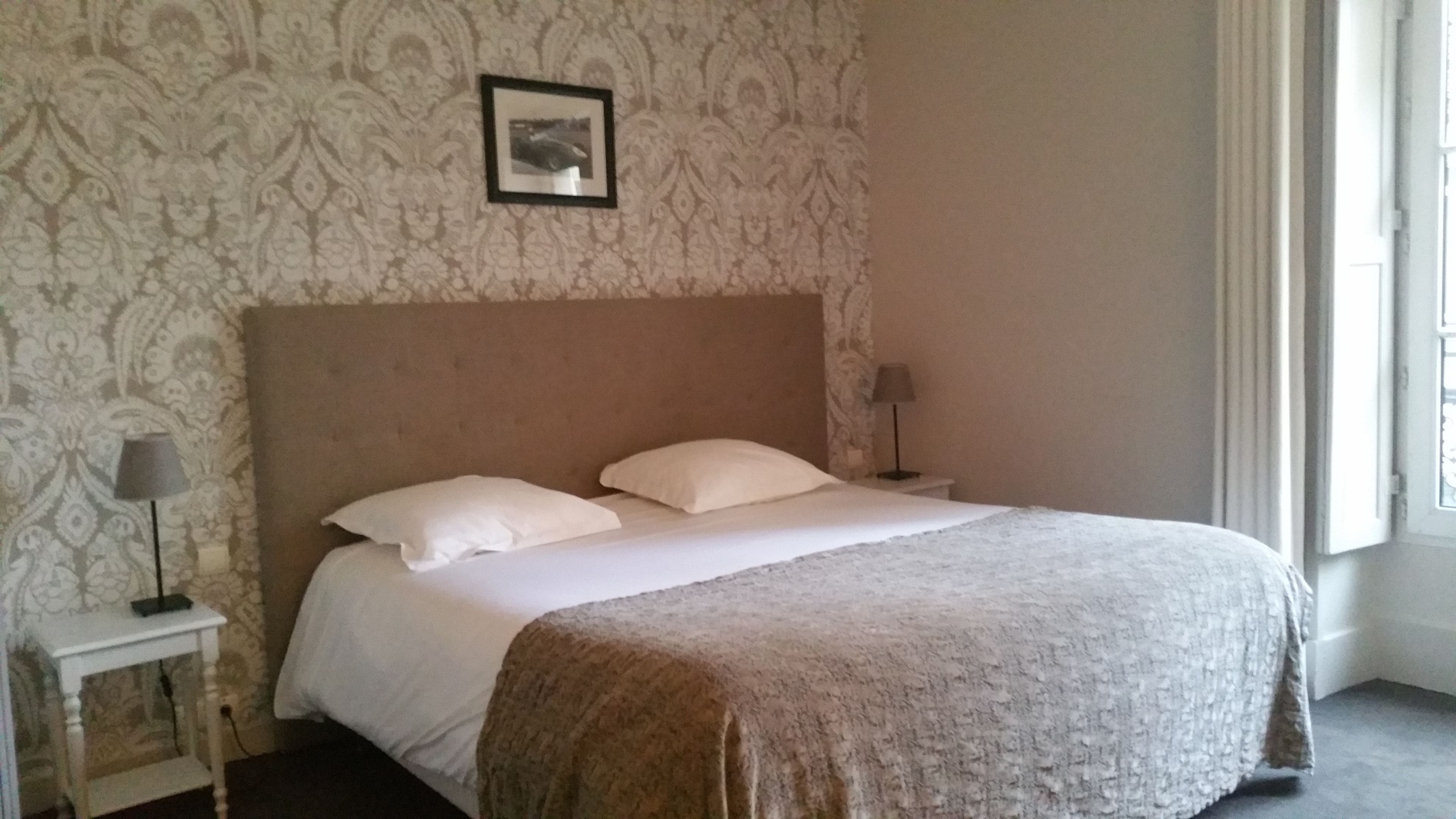 A neatly made bed with a headboard, two bedside tables with lamps, and a patterned wallpaper.