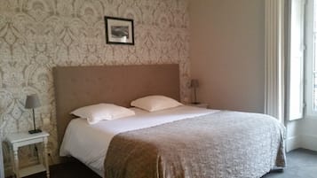 A neatly made bed with a headboard, two bedside tables with lamps, and a patterned wallpaper.