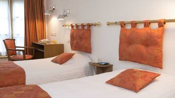 A hotel room with two beds, a desk, a chair, and a nightstand with a lamp and phone.