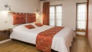 Um quarto espaçoso com uma cama grande, uma mesinha de cabeceira com abajur e uma janela com cortinas.