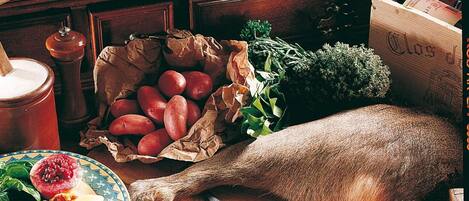 Un ambiente de cocina rústica con diversos alimentos, incluyendo un pescado entero, manzanas y una tarta sobre la mesa.