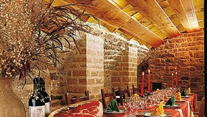 Um restaurante com paredes de pedra, vigas de madeira e mesas postas para uma refeição.