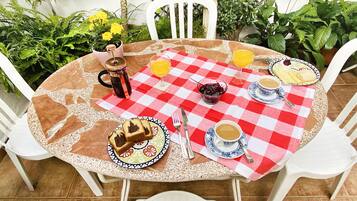 Un área de comedor al aire libre con mantel a cuadros, platos de comida, tazas de café y un termo.