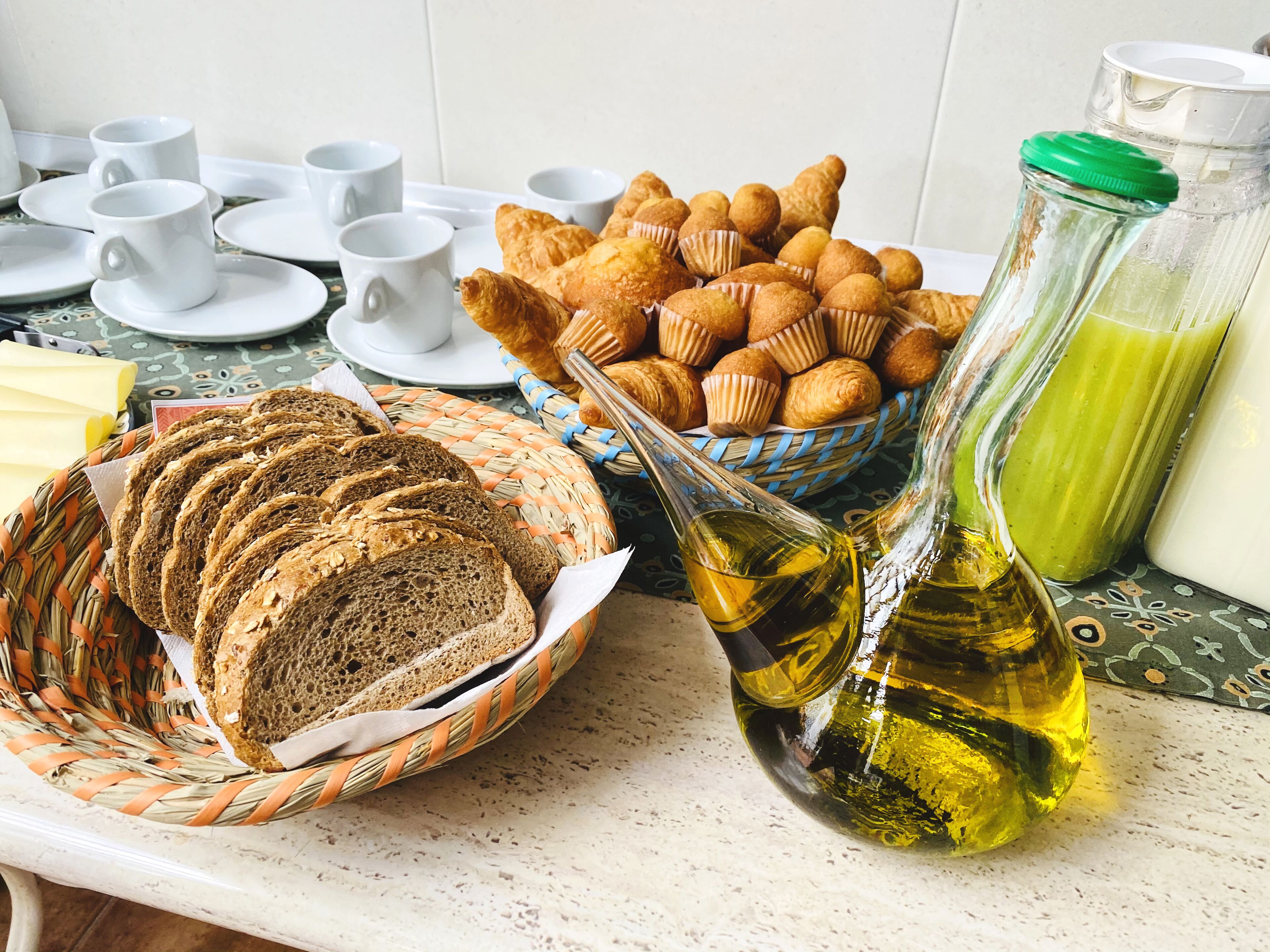 Une table mise pour le petit-déjeuner, avec du pain, des viennoiseries et une bouteille d’huile.