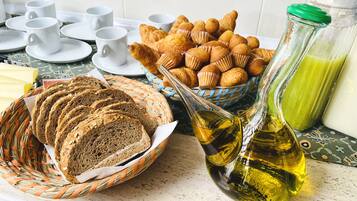 A breakfast setting with bread, pastries, and a bottle of oil on a table.