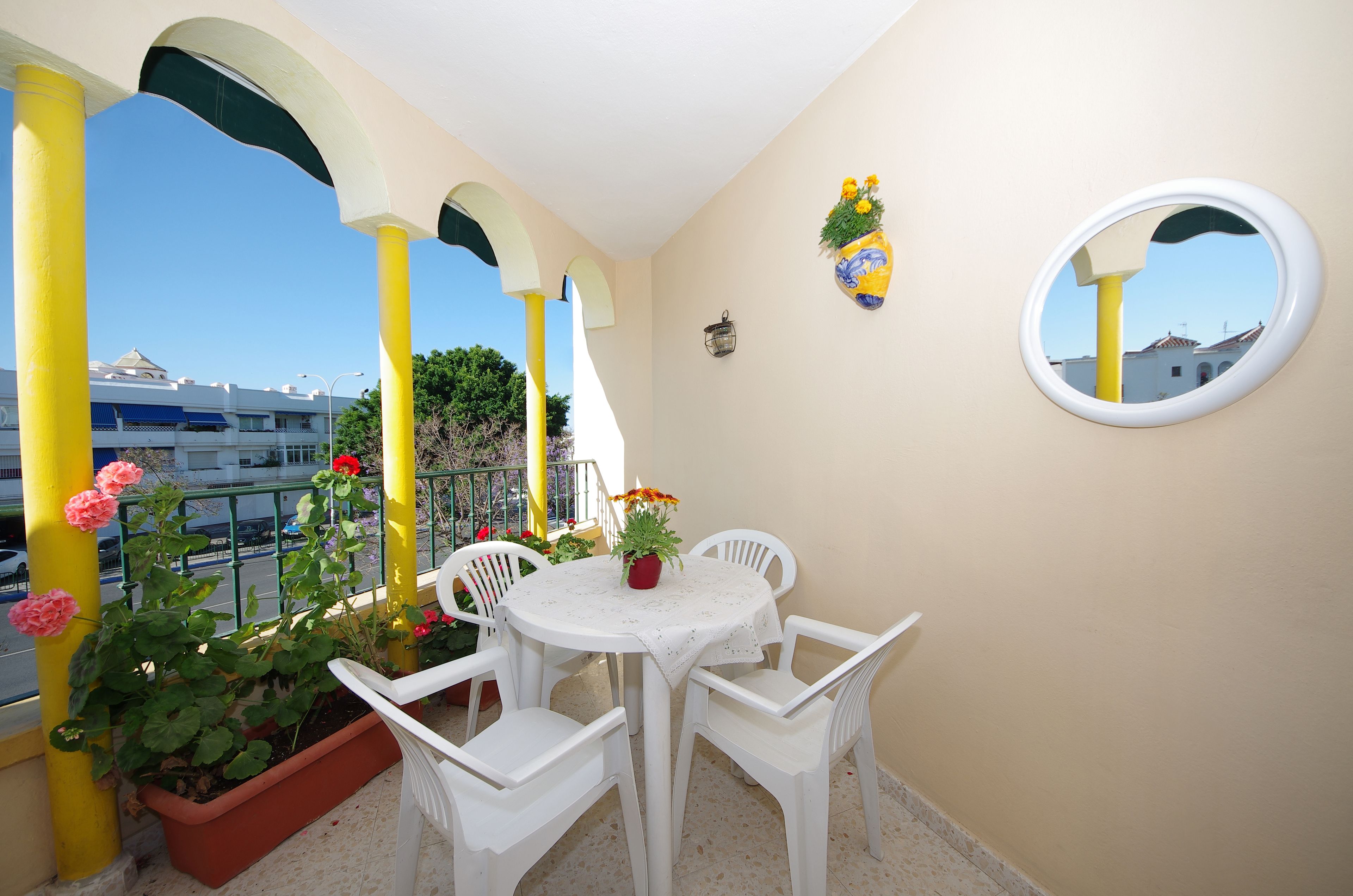 A balcony with white chairs, a round table, and potted plants.
