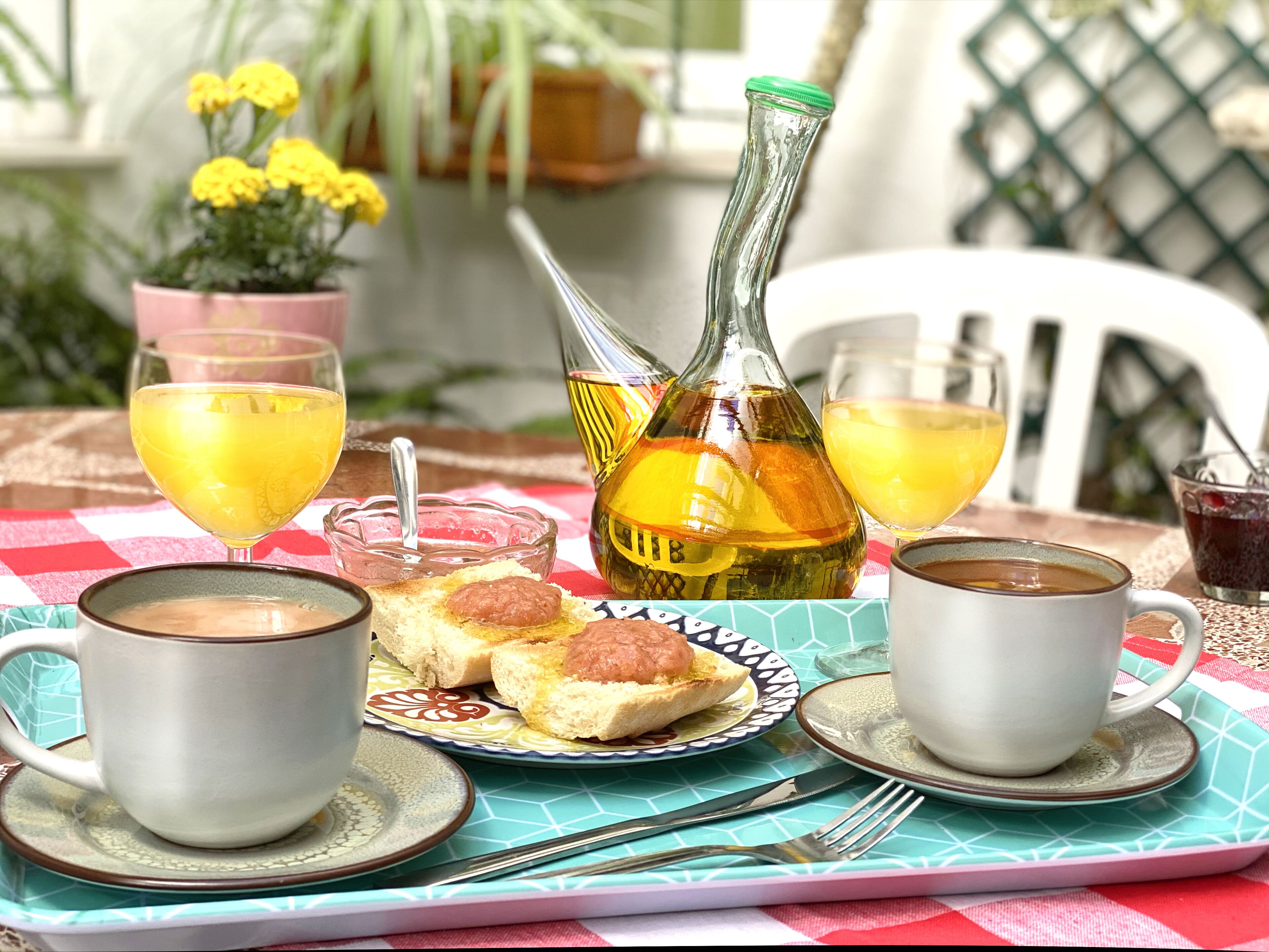 Ein Frühstückstisch für zwei Personen, mit zwei Kaffeetassen, einem Orangensaftglas, einer Orangensaftflasche, einer Toastplatte mit Marmelade und einer kleinen Schale mit Marmelade.