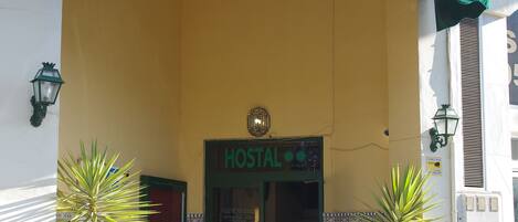 A building with a green awning labeled "HOSTAL AZAHARA" and a sign above the entrance. There are two large potted plants in front of the entrance.