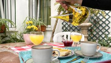 Una mesa con dos tazas blancas, un vaso de jugo de naranja, un vaso de jugo rojo, un plato con tostadas y un tenedor.