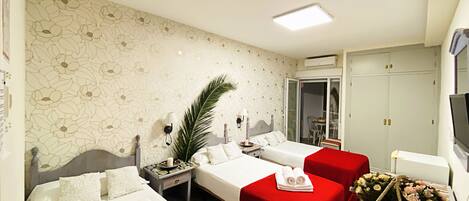 A hotel room with two beds, a small table with a red tablecloth, a potted plant, and a television.