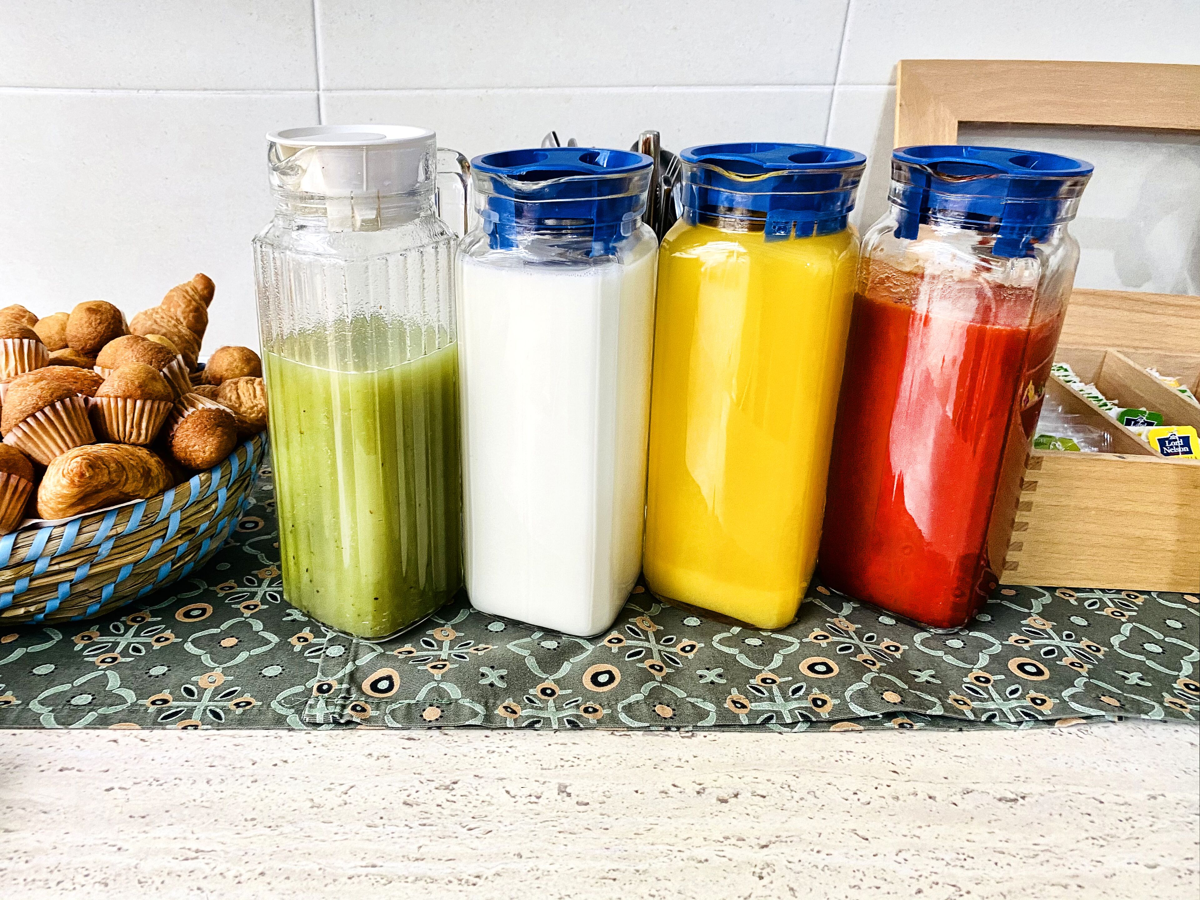 A kitchen counter with a basket of muffins, four bottles of different colored liquids, and a wooden box with snacks.