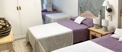 Hotellihuone, jossa on kaksi sänkyä, pieni pöytä, lamppu ja koristeellinen kori.
