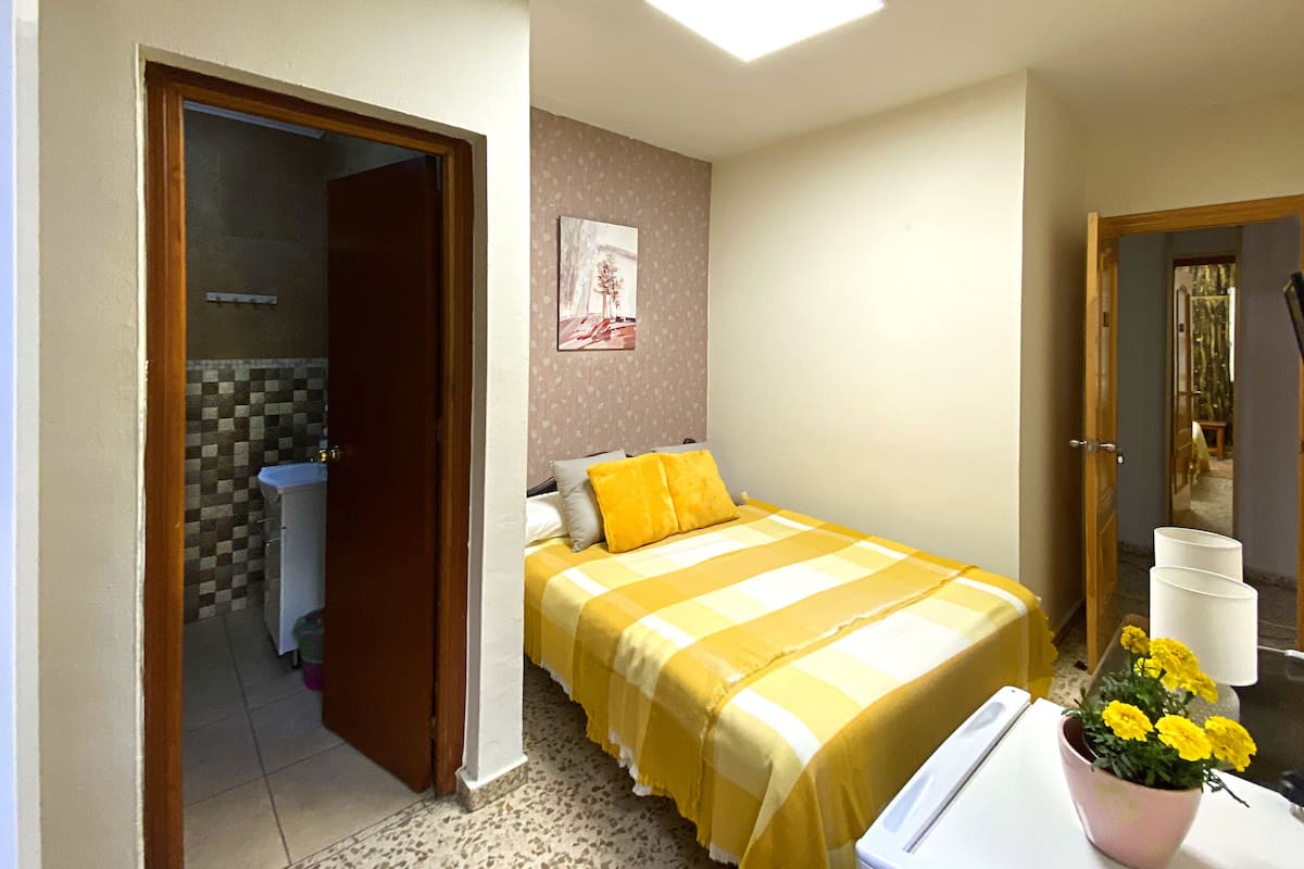 Ein Schlafzimmer mit Bett, Badezimmer und einem kleinen Tisch mit Blumenvase.