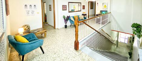 A spacious living area with a blue armchair, a wooden staircase, and a ceiling fan.