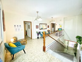 Un amplio espacio de sala con un sillón azul, una escalera de madera y un ventilador de techo.