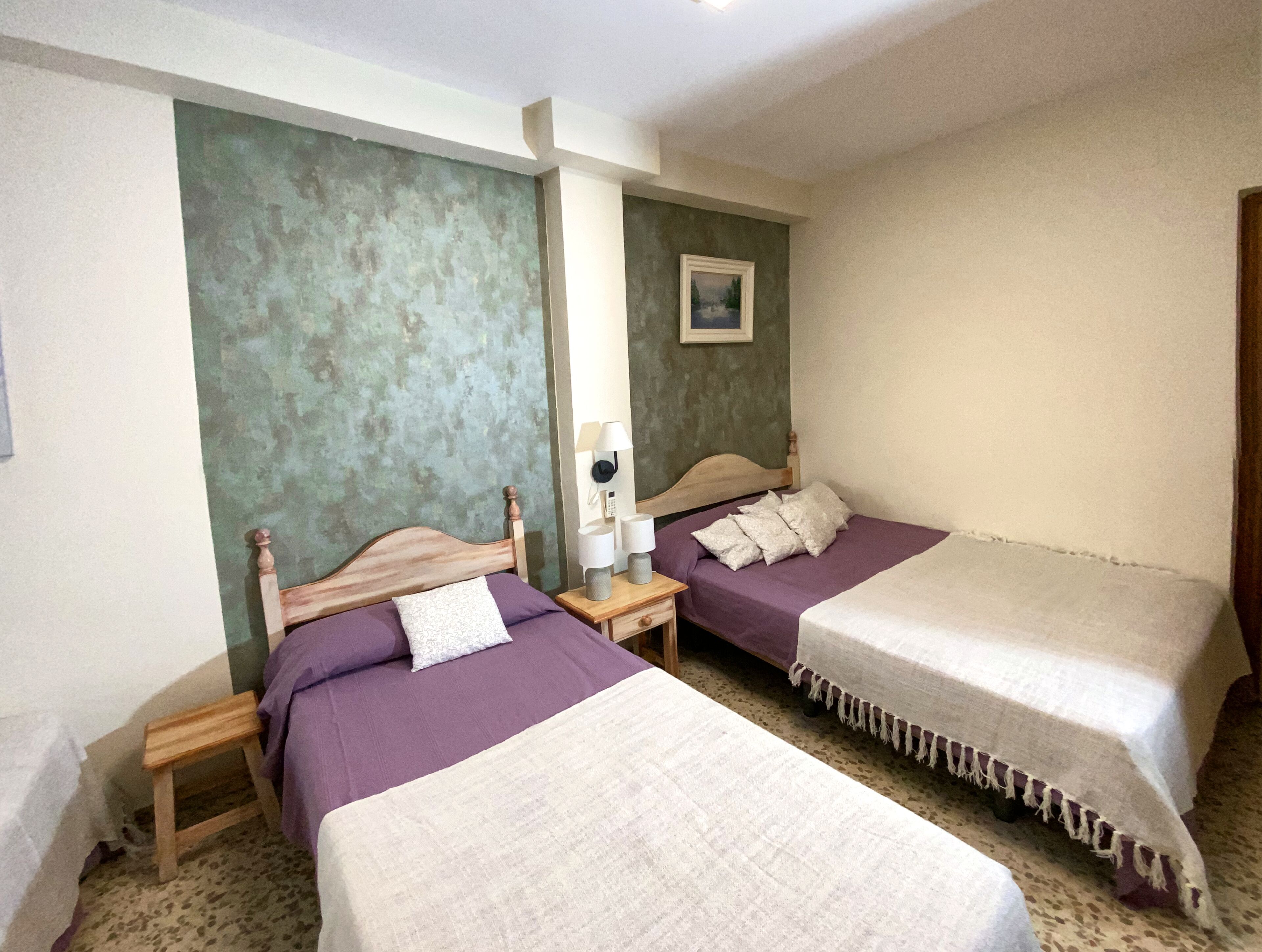 Ein Hotelzimmer mit zwei Betten, jeweils mit einem hölzernen Kopfteil, einem Nachttisch und einer Lampe.