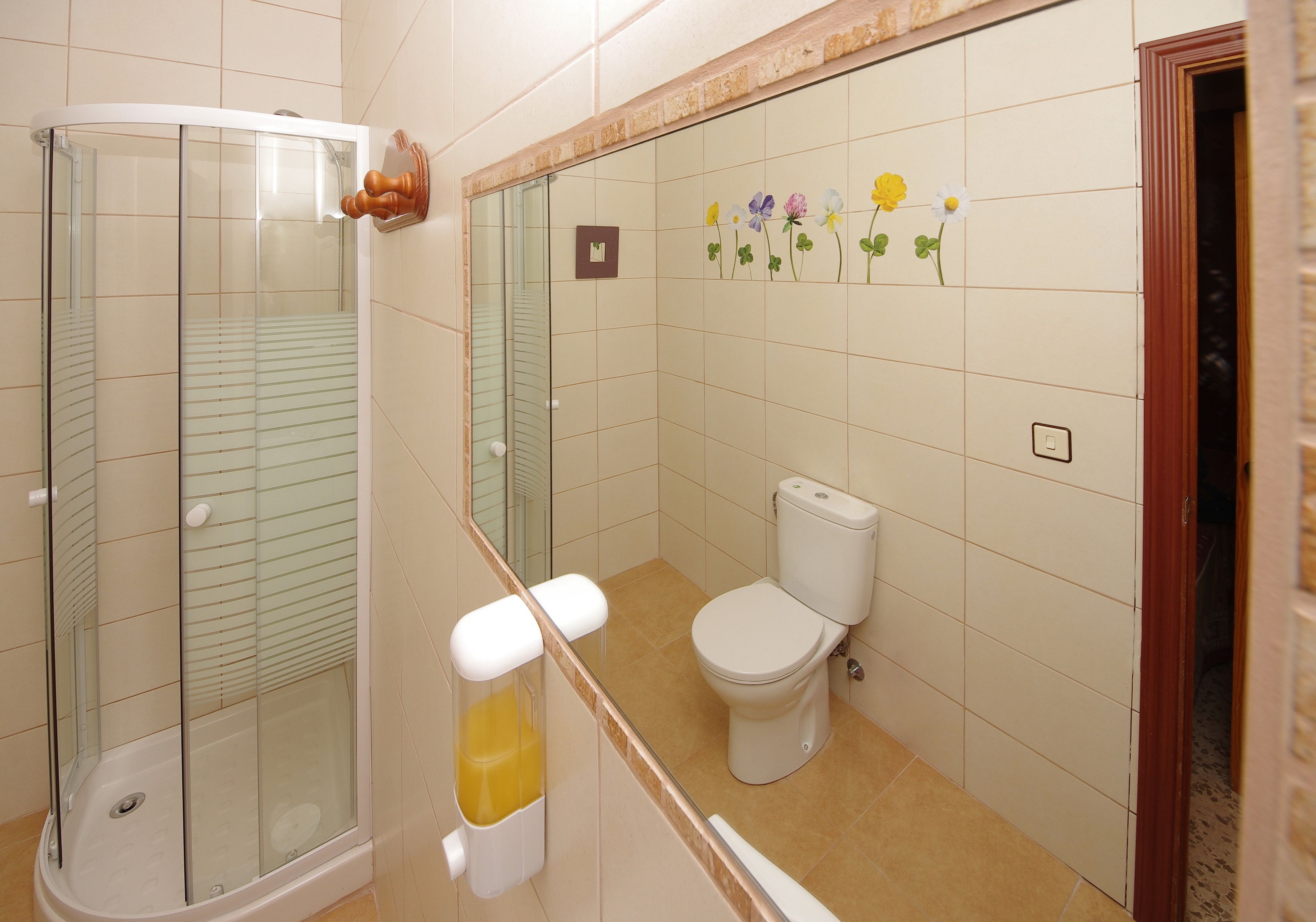 A bathroom with a glass-enclosed shower, a toilet, and a sink with a soap dispenser.