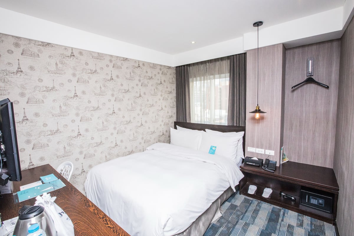 A hotel room with a bed, a desk with a computer, a telephone, and a minibar.