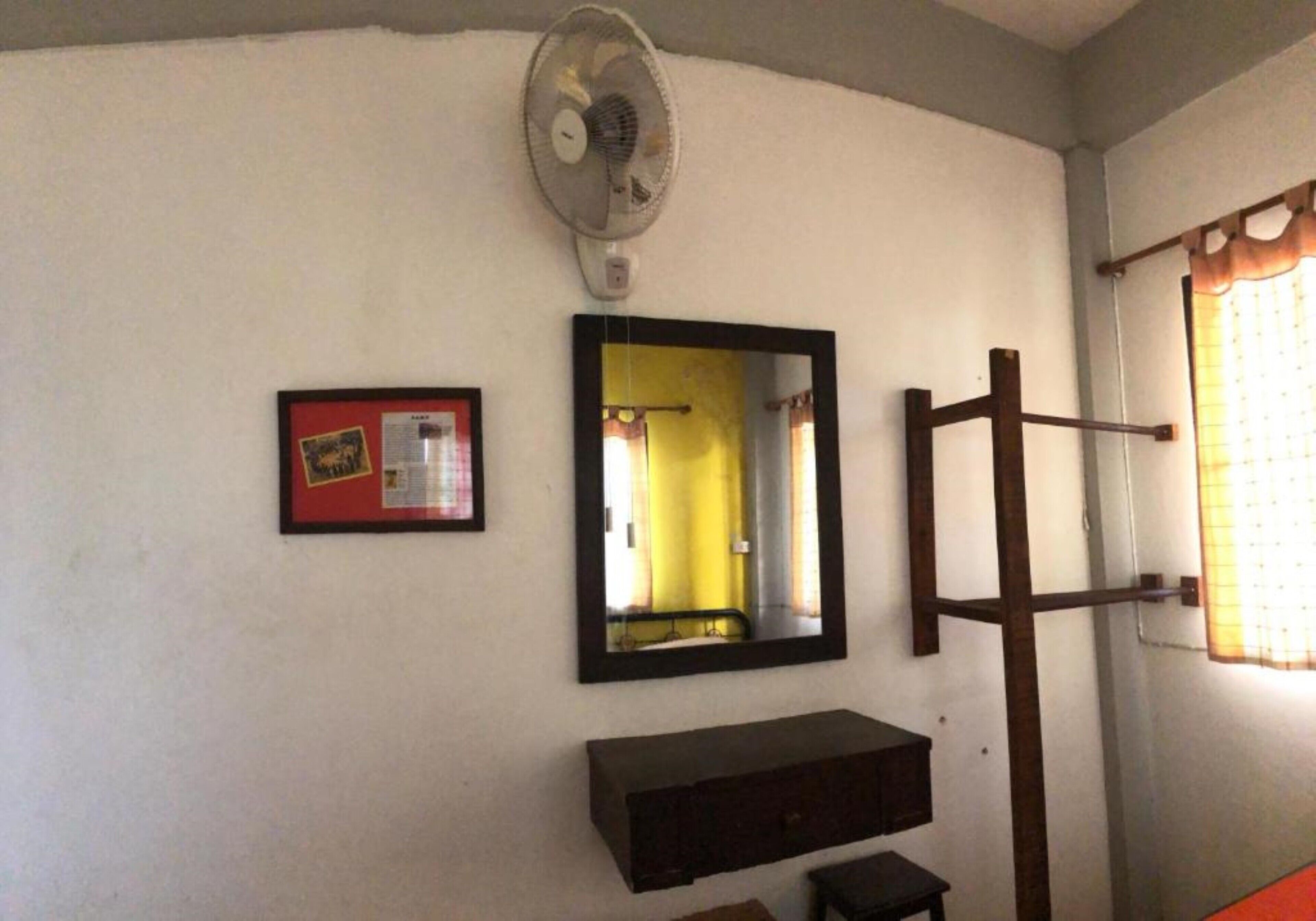 Een kamer met een plafondventilator, een lijstvormig spiegel, een houten rek en een klein plankje.
