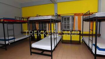 A dormitory room with bunk beds, yellow walls, and a window with curtains.