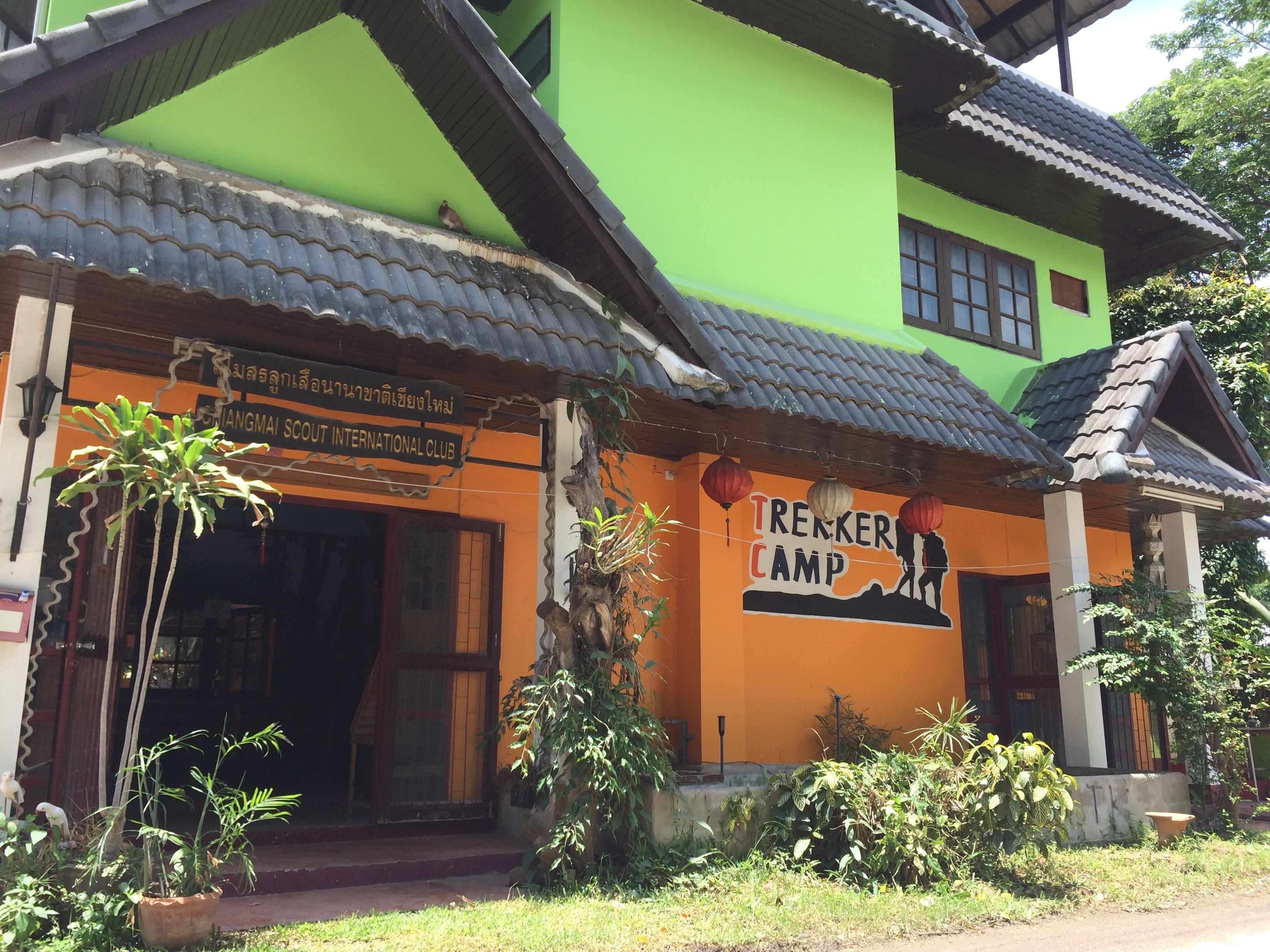 A building with a green and orange facade, a tiled roof, and a sign for 'Trekker Camp'.