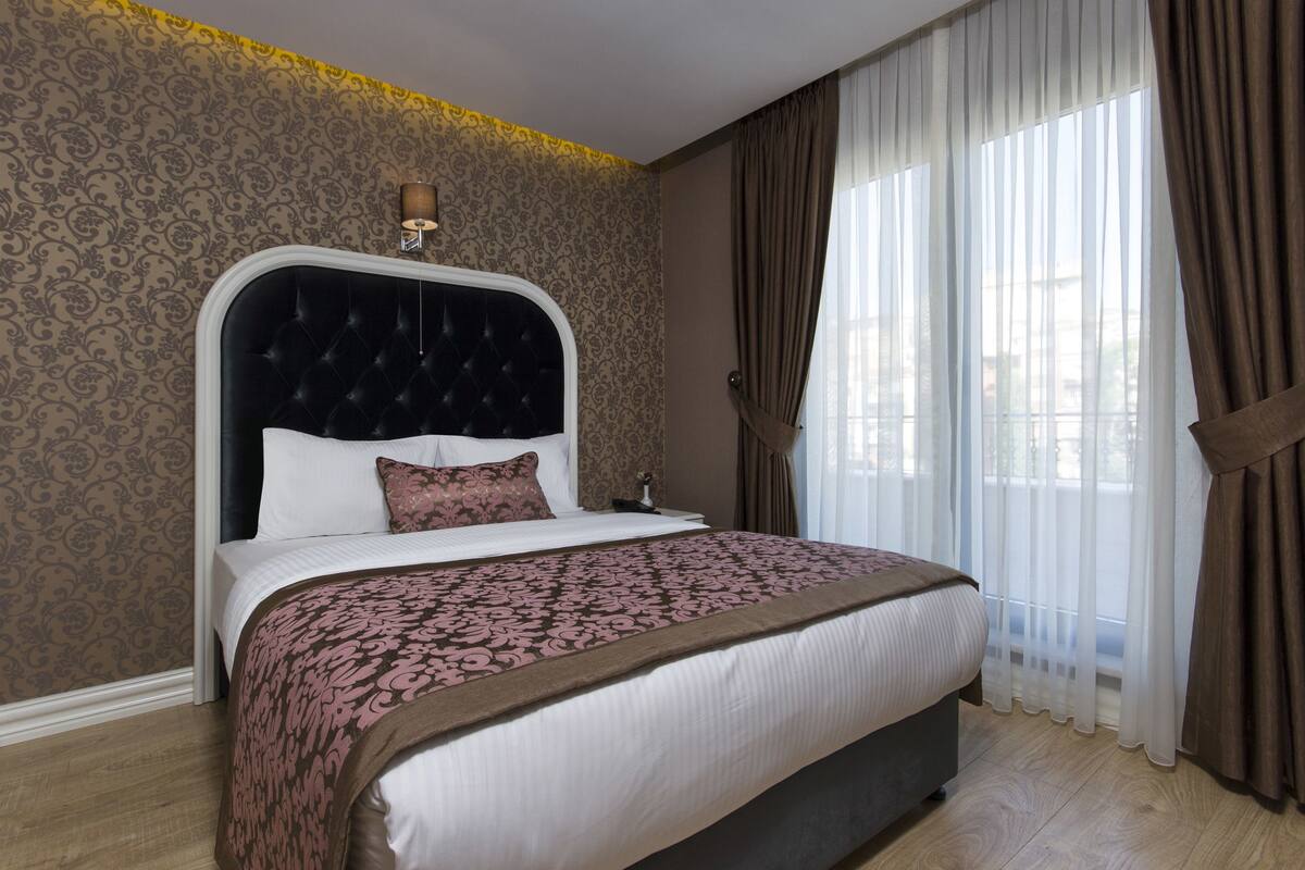 A neatly made bed with a patterned bedspread, a tufted headboard, and a bedside lamp.