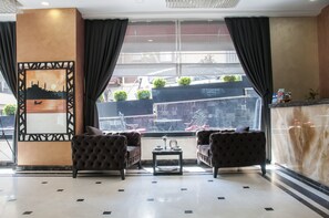 A lobby with two tufted armchairs, a small table, and a large window with curtains.