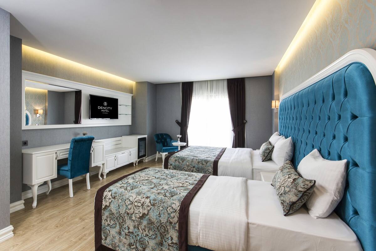 A hotel room with two beds, a desk, a chair, and a television.
