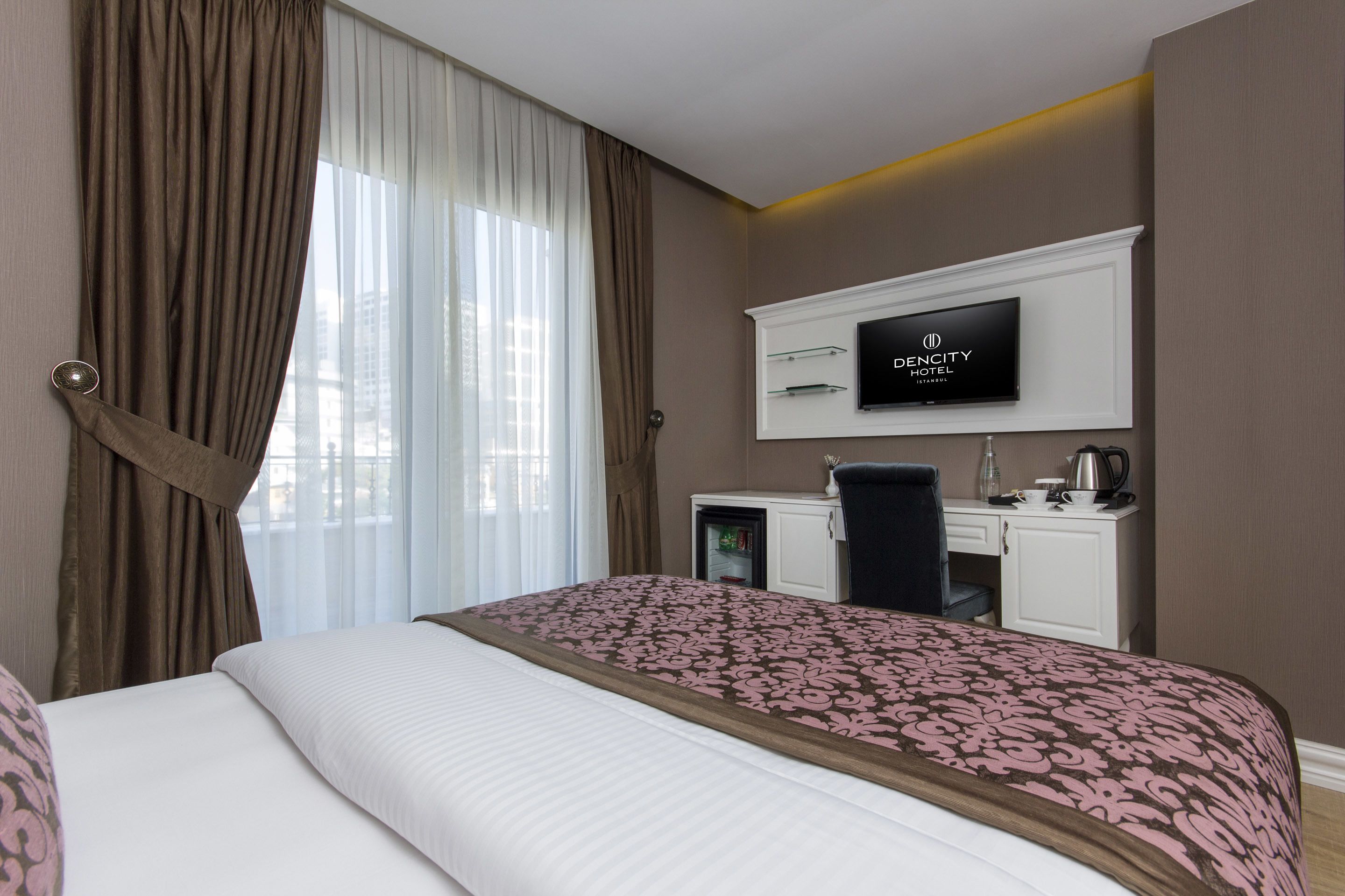 Een hotelkamer met een bed, een bureau, een televisie en uitzicht op de stad.