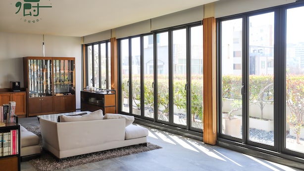 Una habitación de hotel moderna con un ventanal grande, un sofá, un armario de madera y una estantería.