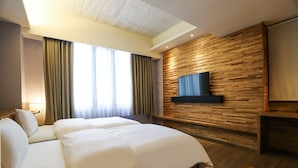 Habitación de hotel con dos camas, un televisor montado en una pared de madera y un ventanal con cortinas.