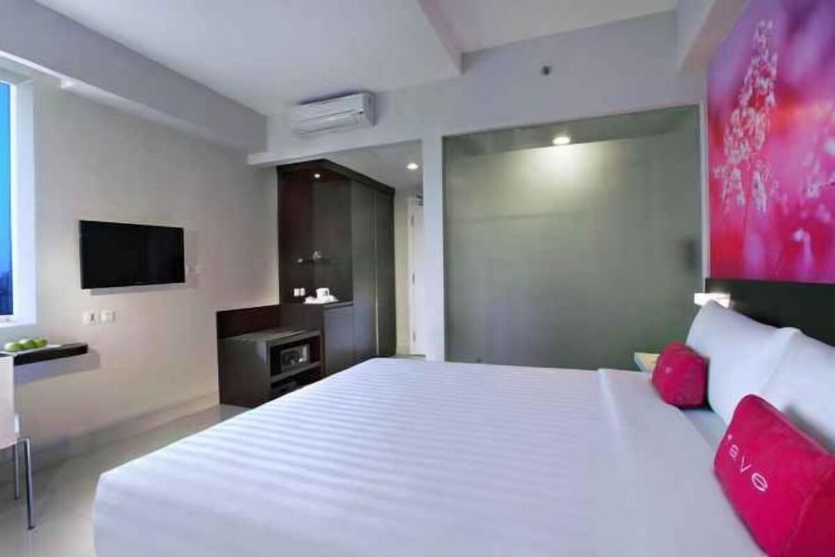Une chambre d’hôtel moderne équipée d’un grand lit, d’un téléviseur à écran plat, d’un bureau et d’un climatiseur fixé au mur.