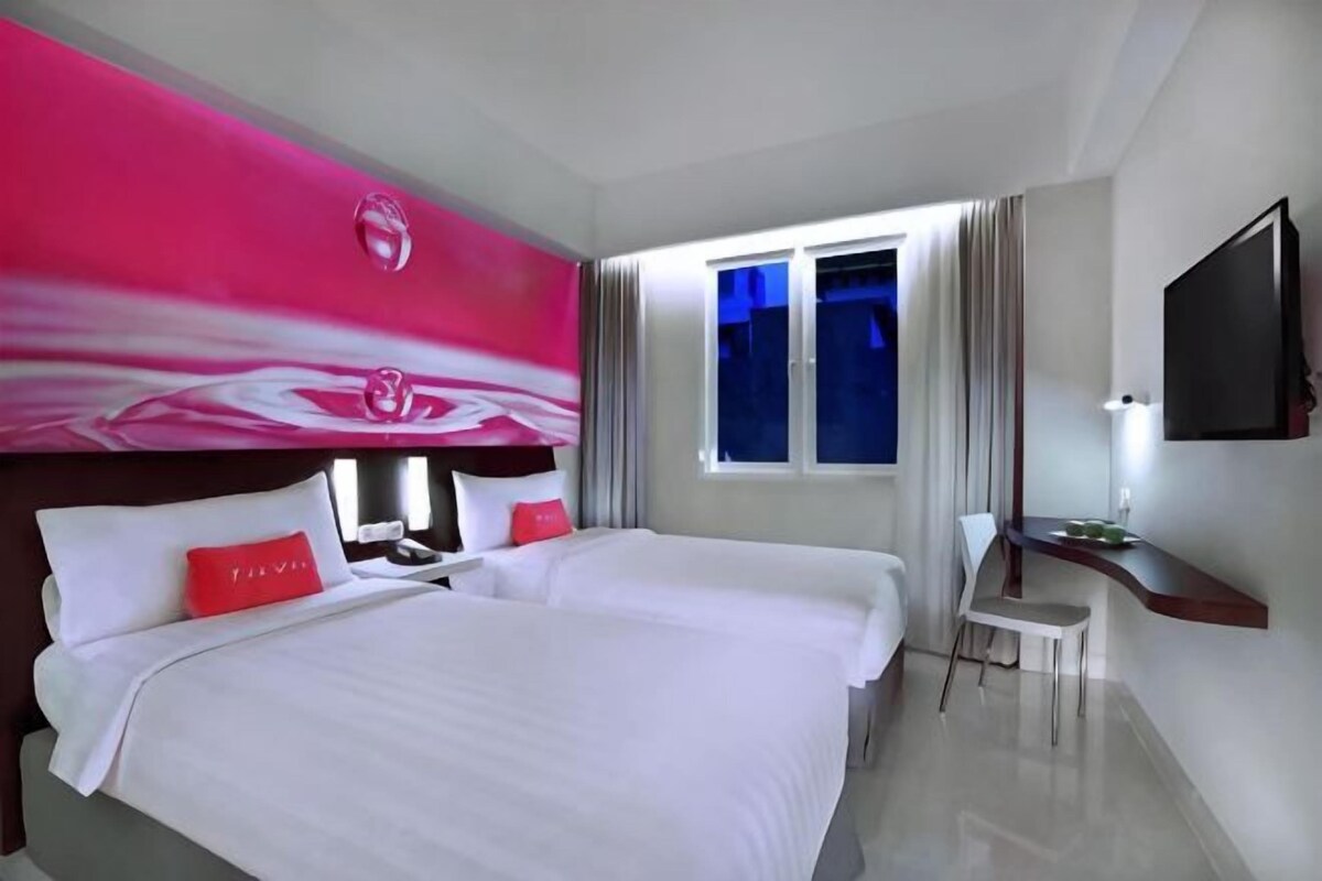 Une chambre d’hôtel avec un grand lit, un bureau, une télévision et une fenêtre avec des rideaux.