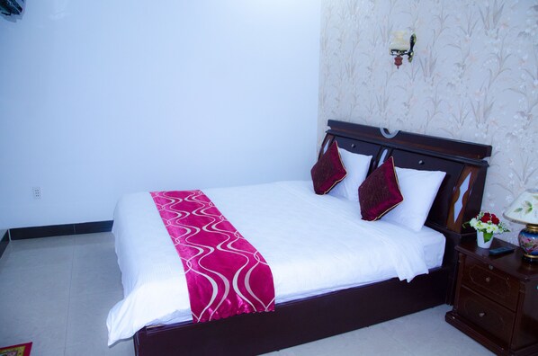 A neatly made bed with a white and pink bedspread, two red pillows, and a wooden headboard. - Salina Hotel (Da Nang)