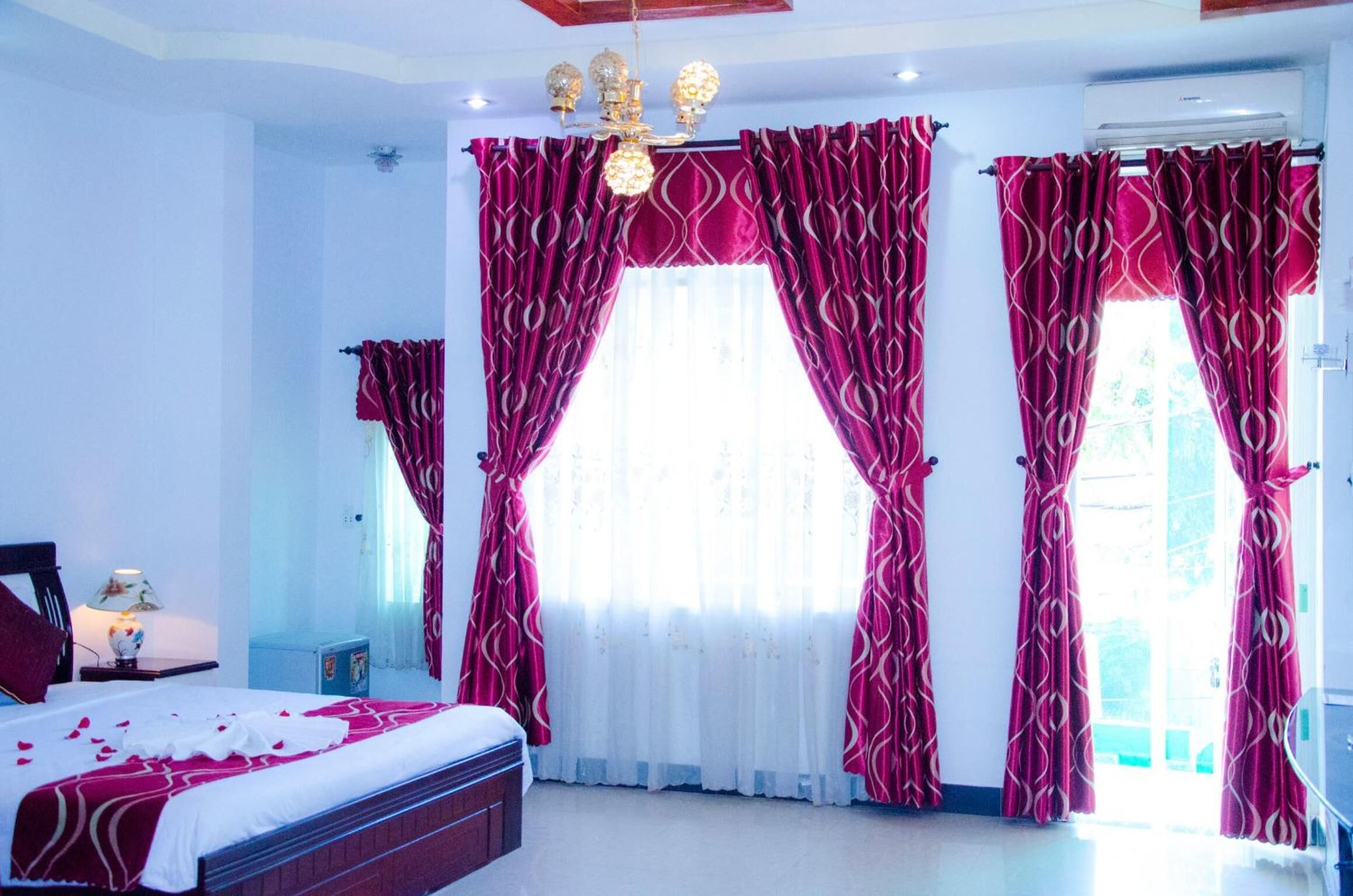 Quarto com cama, cortinas, um lustre e janela.