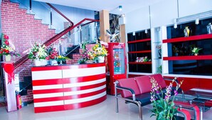 Una zona de recepción con mostrador a rayas rojas y blancas, un refrigerador de Coca-Cola, una escalera y un área de estar con sillas rojas y una mesa.