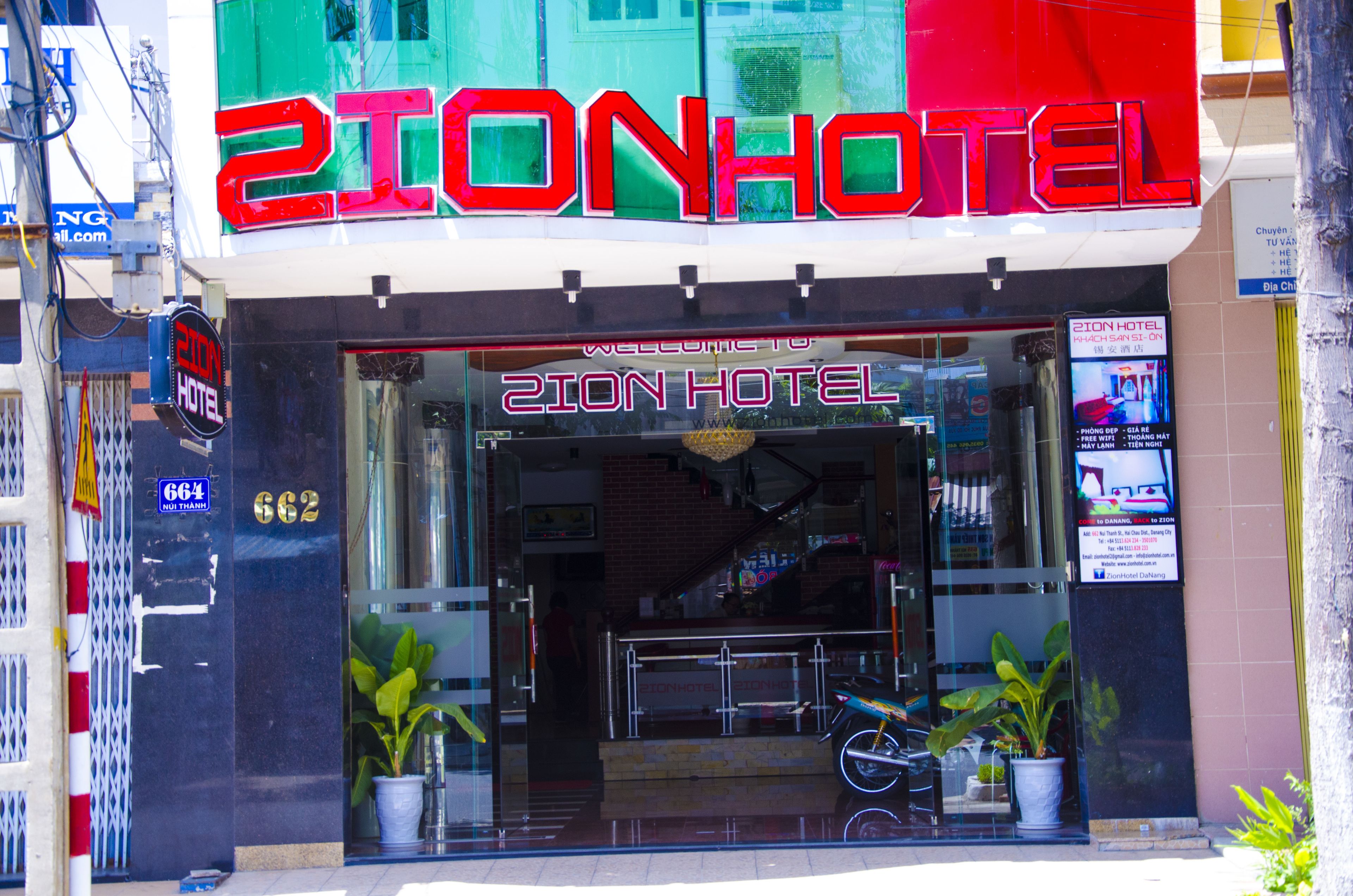The exterior of the 2ION HOTEL with a prominent sign, a glass entrance, and a motorcycle parked outside.