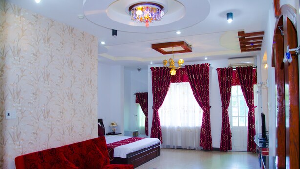 Una habitación de hotel con una cama, un sofá rojo, una mesa de centro de cristal y cortinas rojas.