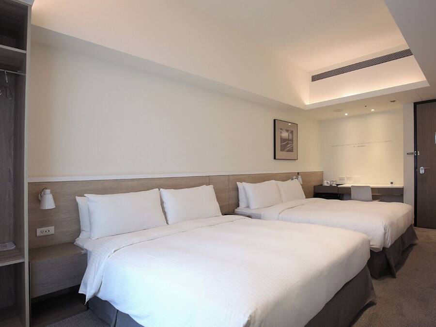 A hotel room with two beds, a desk, a chair, a wardrobe, and a ceiling light.