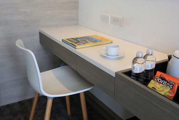 A small kitchenette with a white chair, a cup, a book, two bottles, and a bag of Doritos. - Cityinn Hotel Plus Fuxing N. Rd. Branch (Taipei)