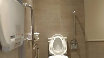 A modern bathroom with a toilet, hand dryer, and trash bin.