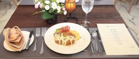 A dining table set with a plate of food, cutlery, a glass of water, a menu, and a small flower arrangement.