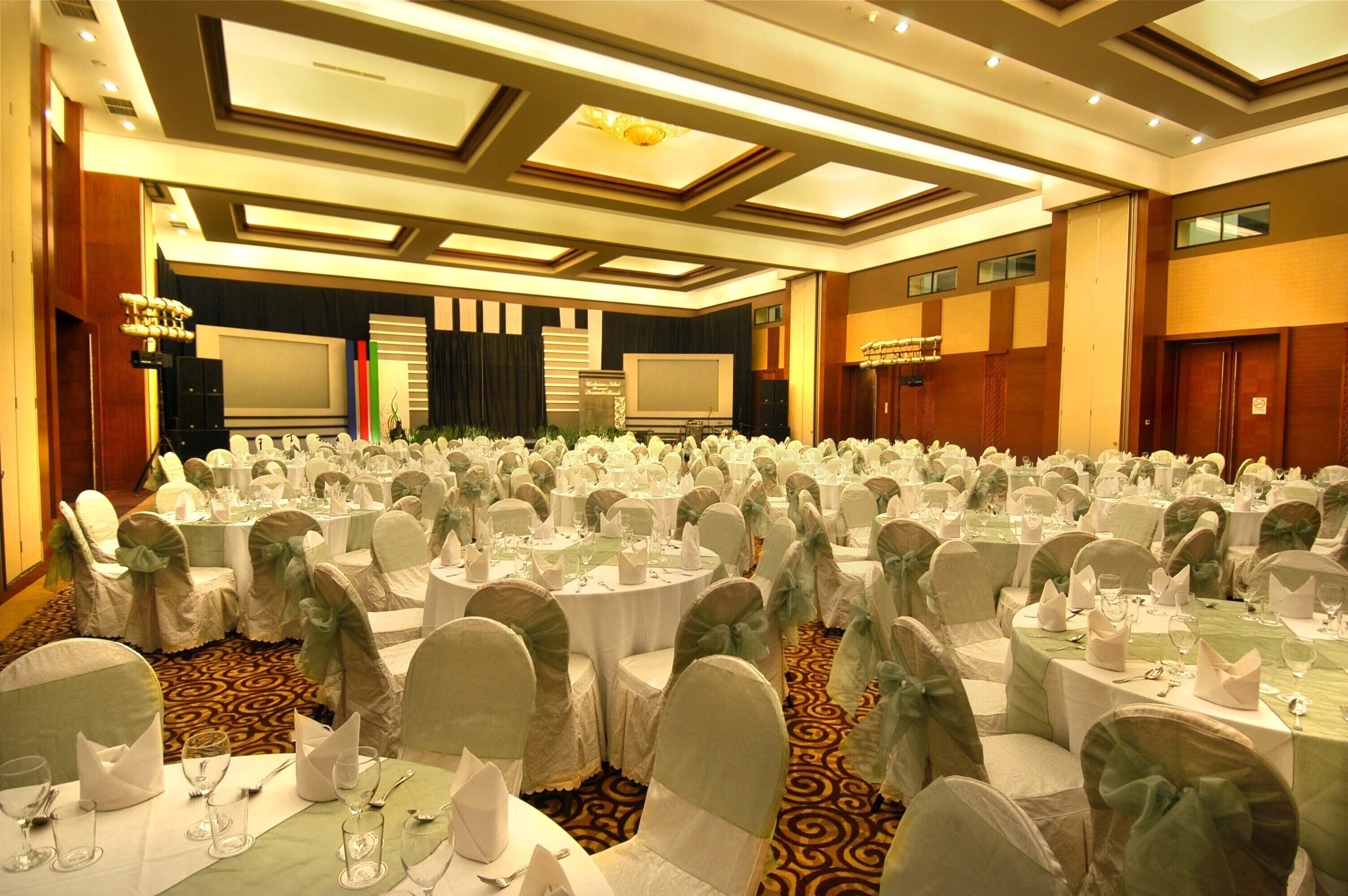 A banquet hall with round tables, white tablecloths, and chairs with green sashes.